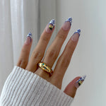 Hand with decorative nail art and a gold ring on a neutral background