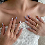 Close-up of hands with decorative nails and gold rings against a neutral background