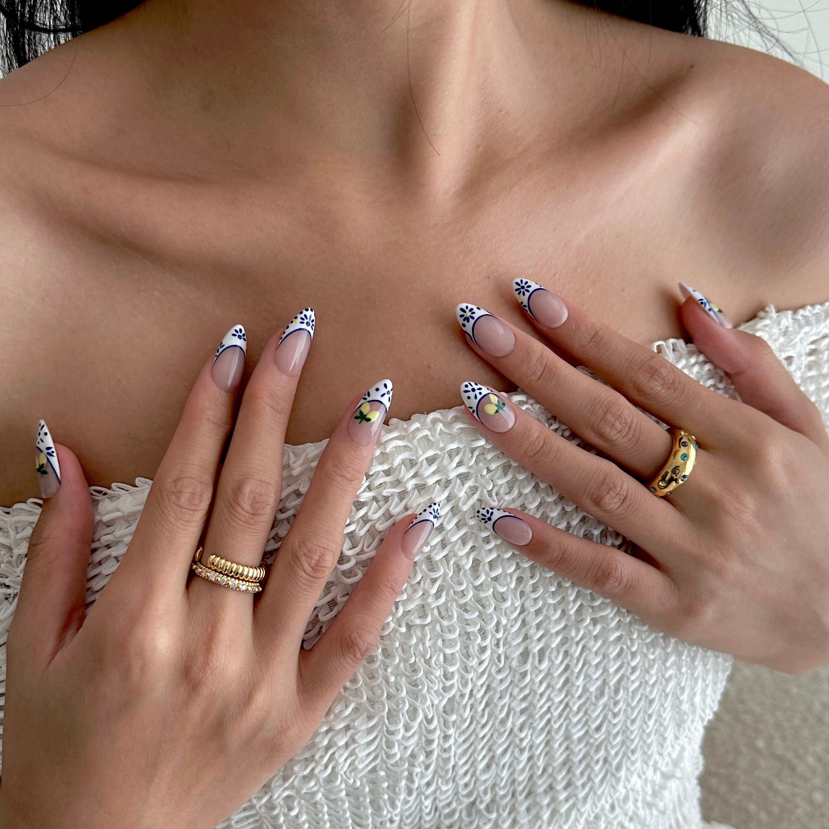Close-up of hands with decorative nails and gold rings against a neutral background
