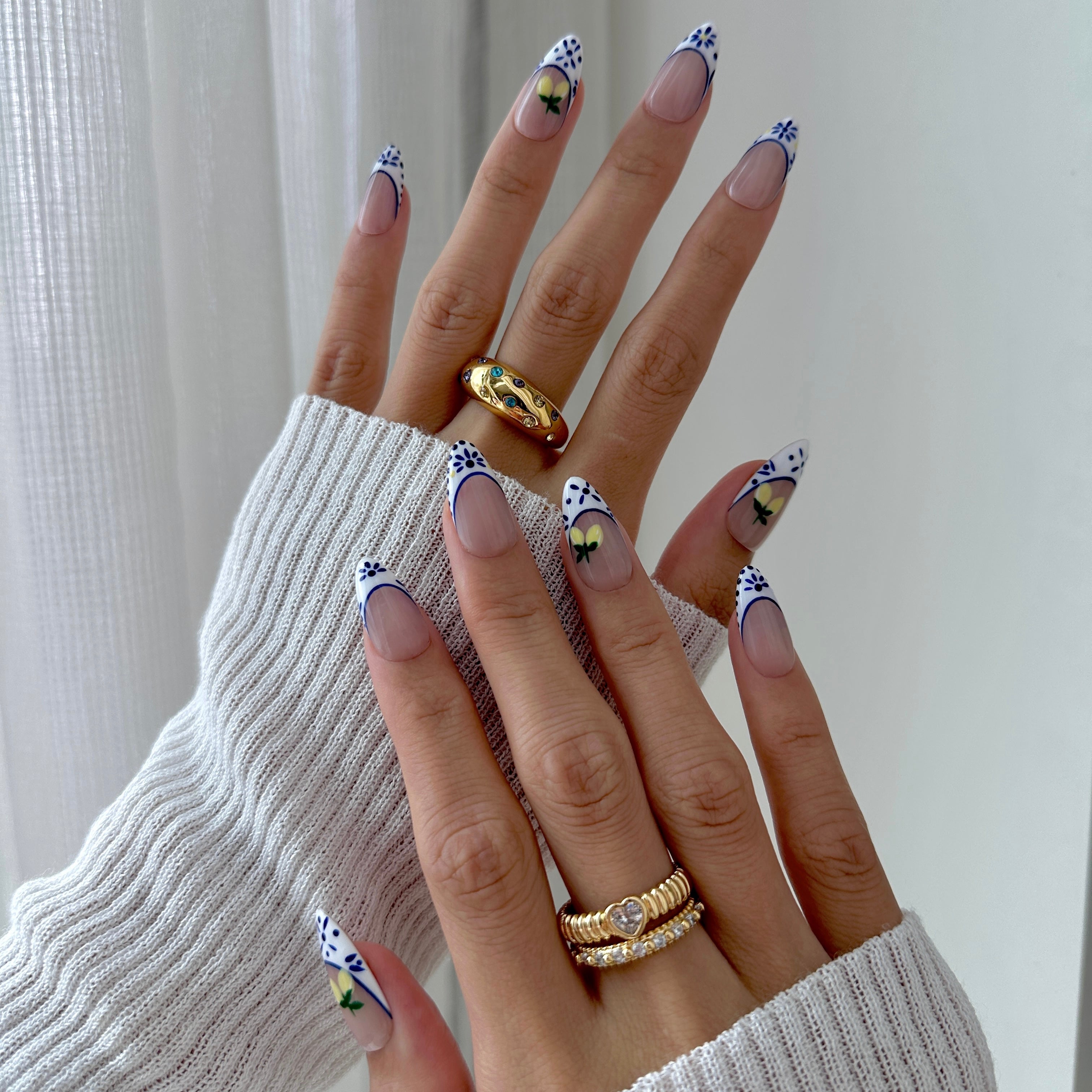 Close-up of a hand with decorative nails and gold rings against a neutral background