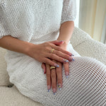 Close-up of a person's hands with rings and nail art on a neutral background