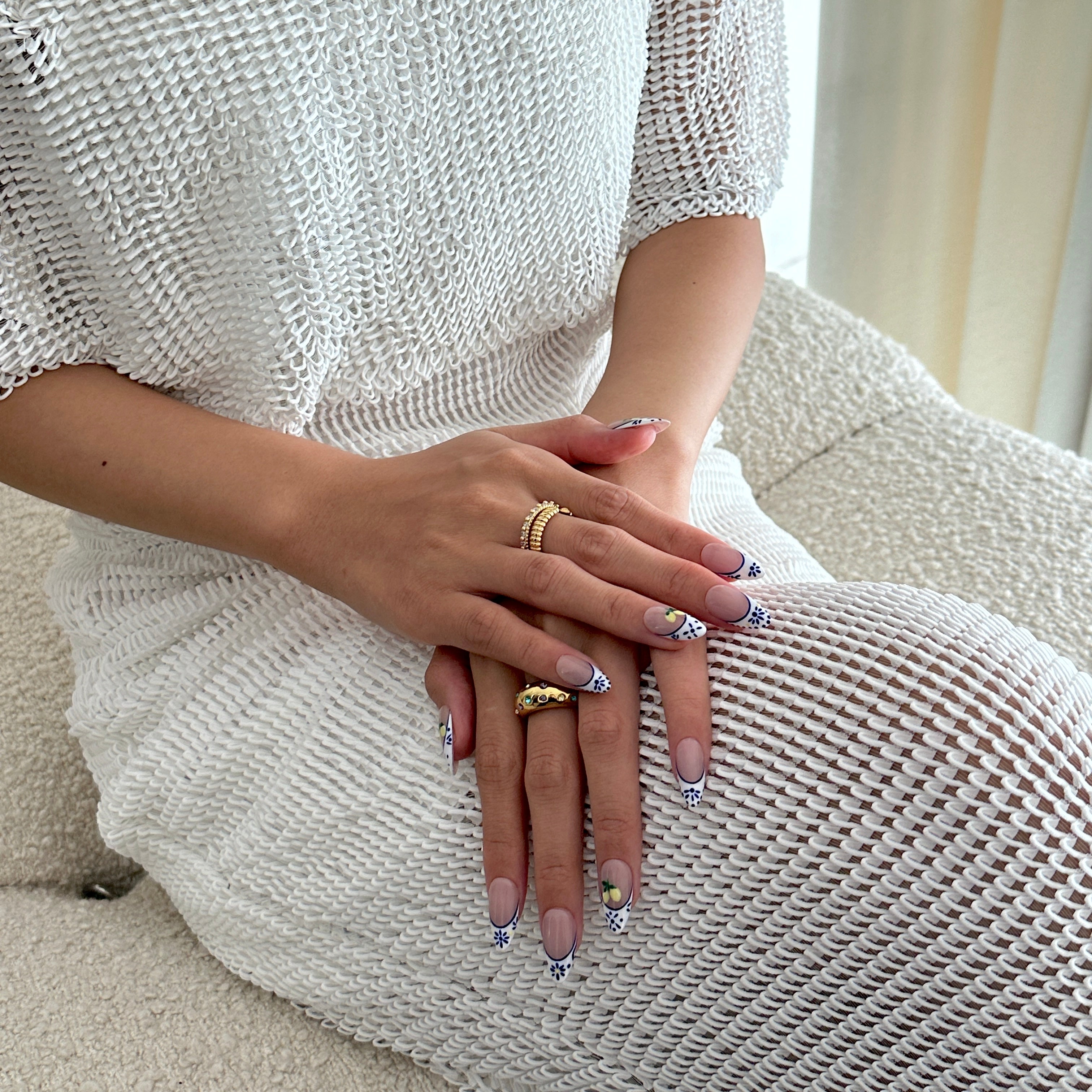 Close-up of a person's hands with rings and nail art on a neutral background