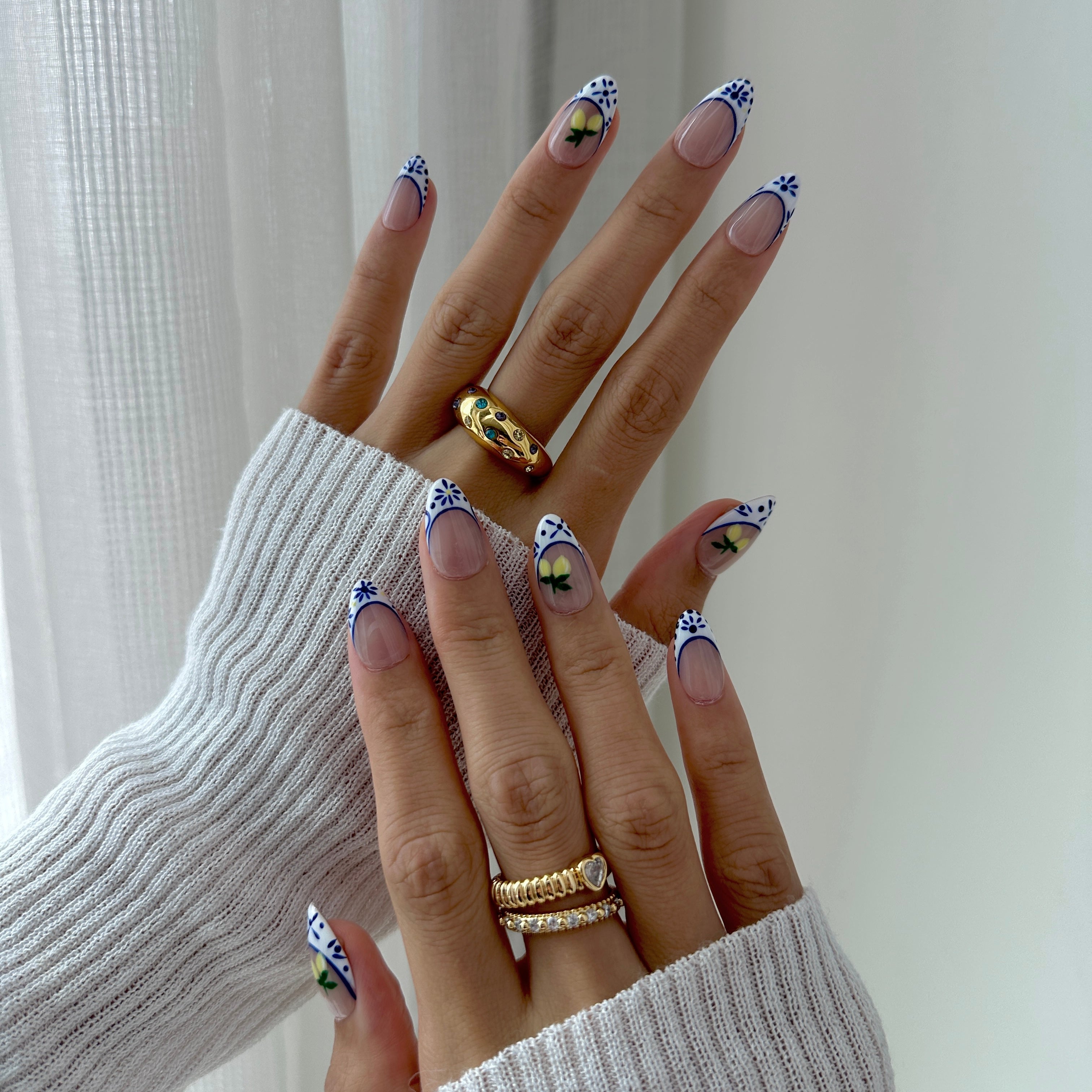 Close-up of hands with decorative nail art and gold rings against a neutral background