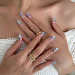 Close-up of hands with decorative nail art and gold rings on a neutral background