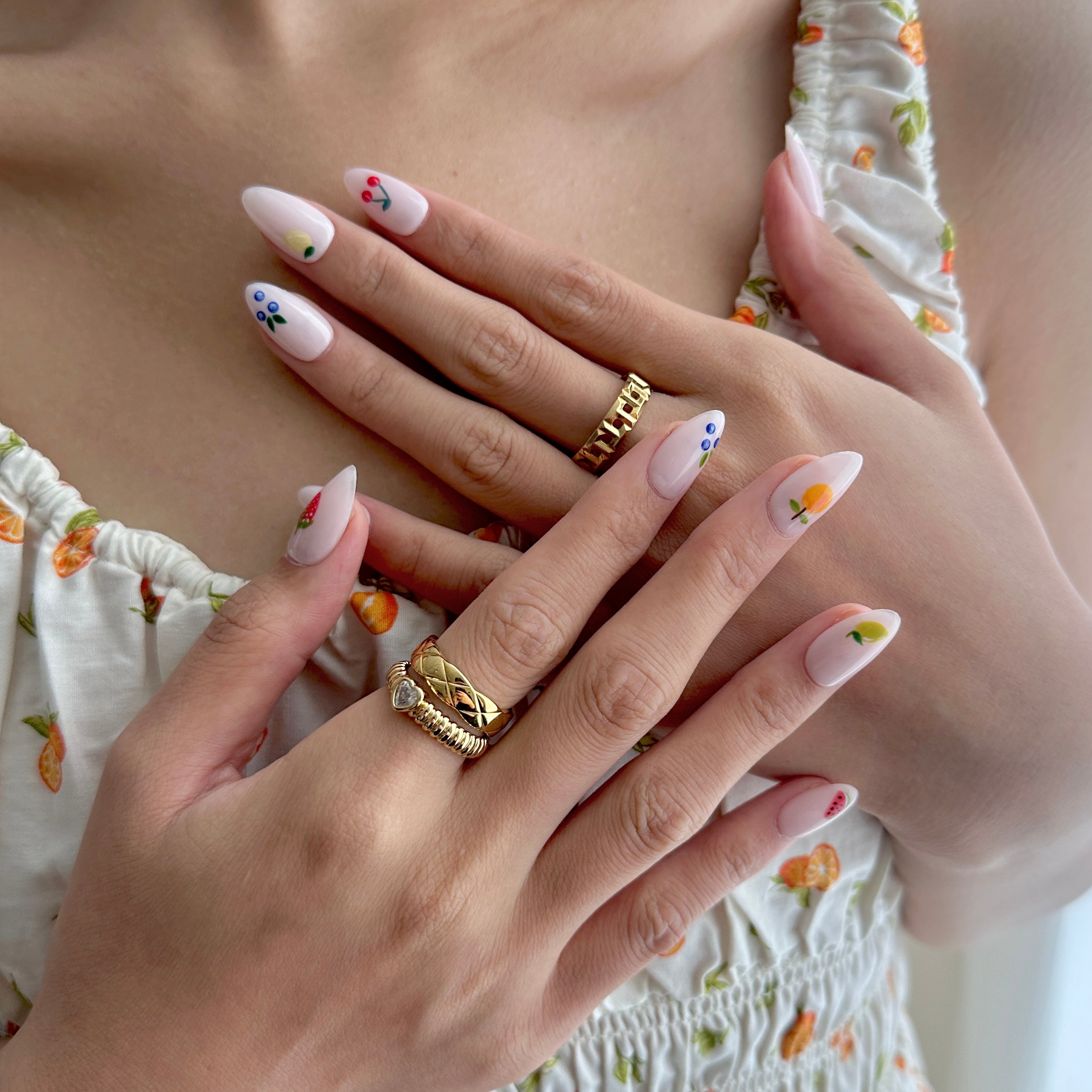 Close-up of hands with floral nail art and gold rings, wearing a floral dress.