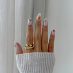 Hand with floral nail art wearing a gold ring against a neutral background
