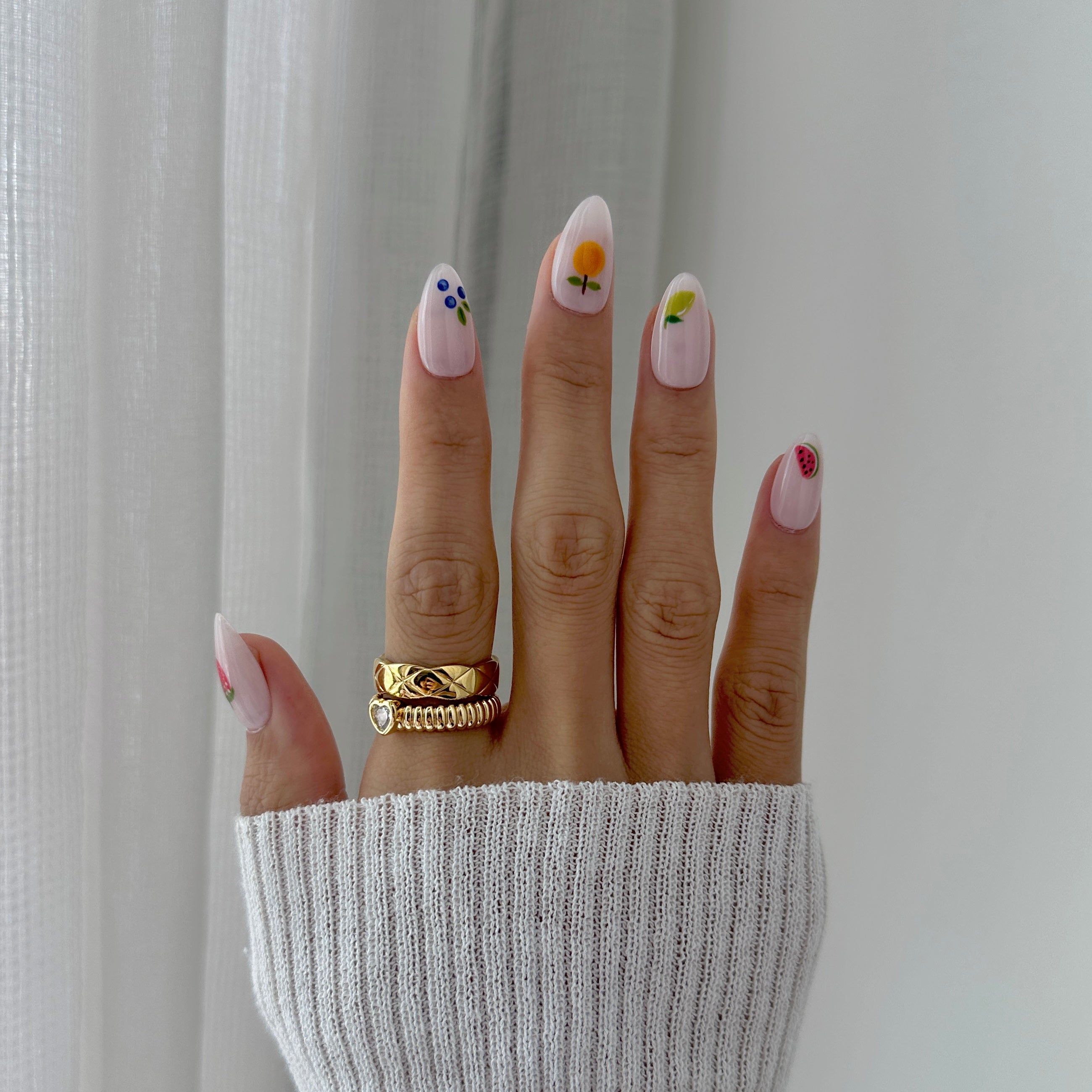 Hand with floral nail art wearing a gold ring against a neutral background
