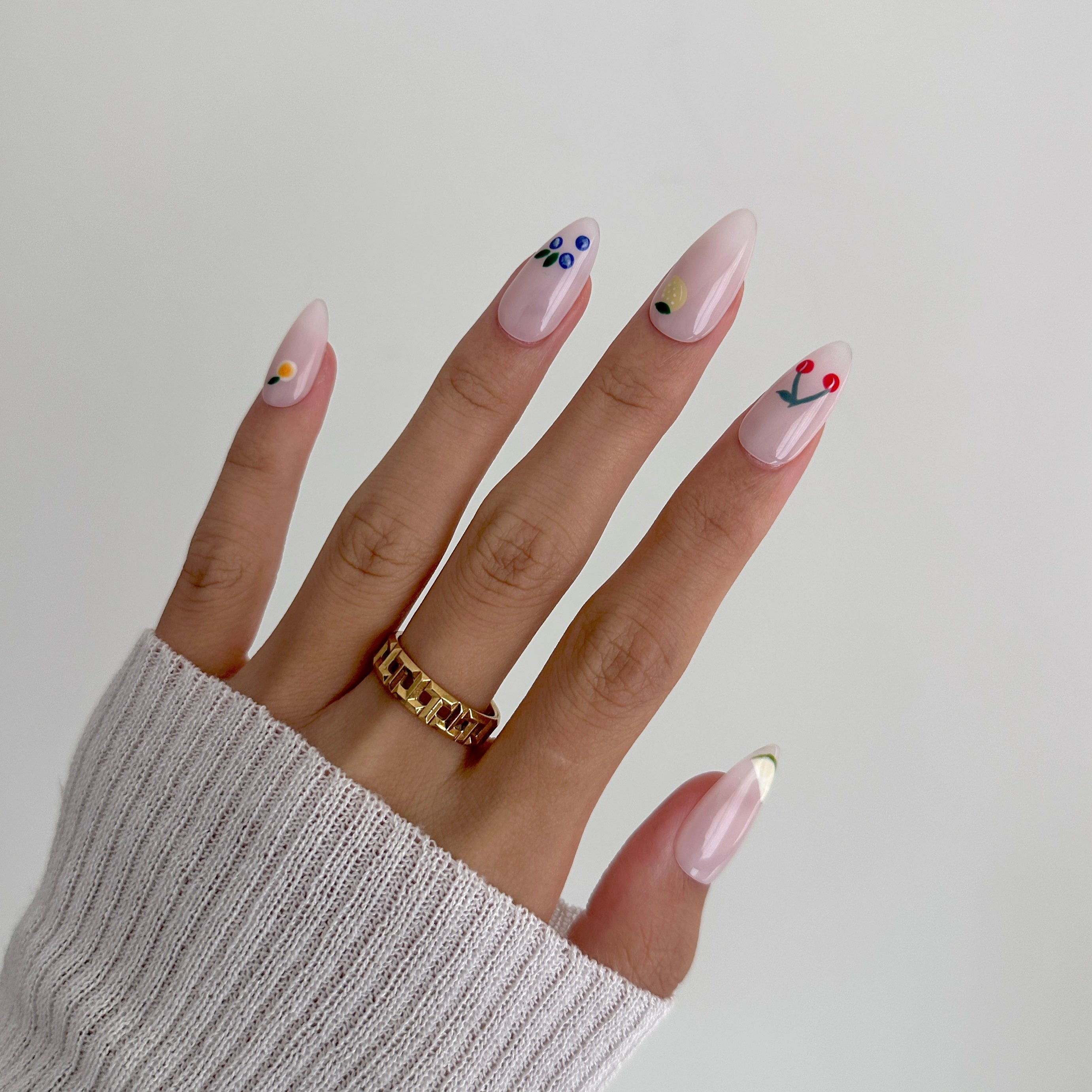 Hand with pink nail art and a gold ring on a plain background