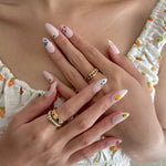 Close-up of hands with decorative nail art and gold rings, wearing a floral dress.