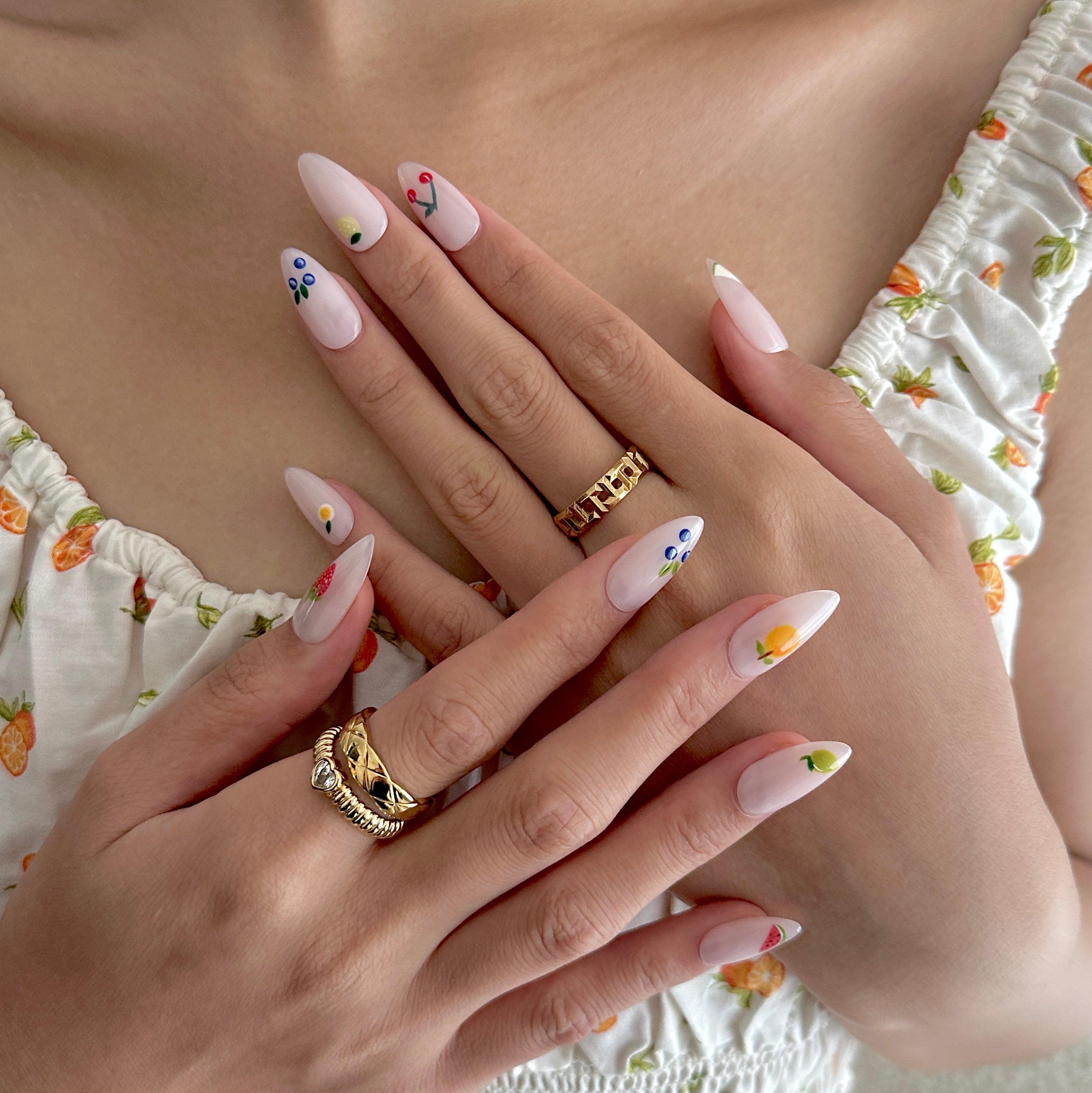 Close-up of hands with decorative nail art and gold rings, wearing a floral dress.