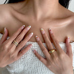 Close-up of a person's hands with handmade press on nails and gold rings, wearing a white textured garment.
