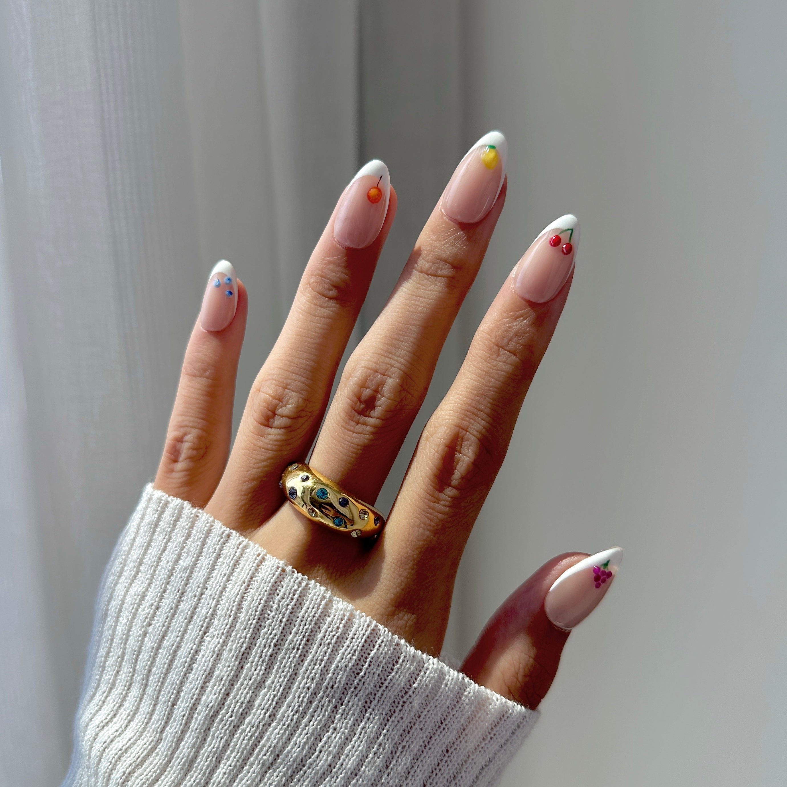 Hand with decorative nails and a gold ring on a neutral background