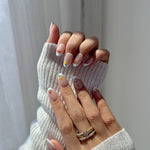 Close-up of a hand with stylish nail art wearing a white textured sleeve.