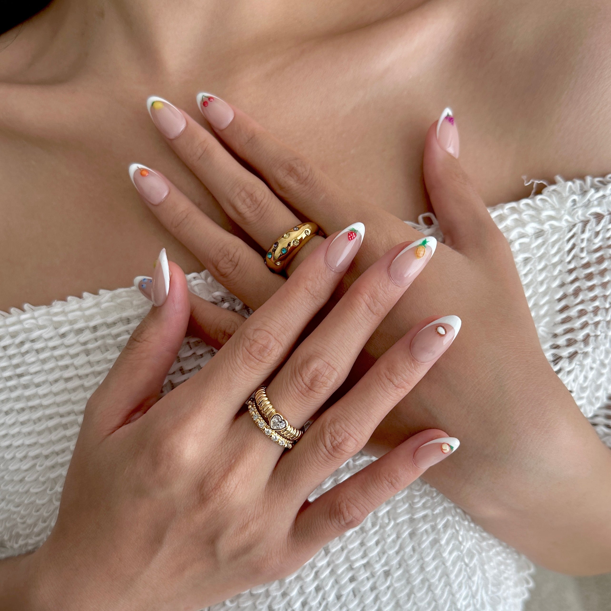 Close-up of hands with press on nails and gold rings on a textured white surface