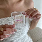 Person holding a clear case with nail art designs, wearing a white textured top.