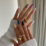 Close-up of a hand with colorful nail art and multiple rings on a neutral background