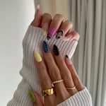 Close-up of hands with colorful nail art wearing a textured white sweater.