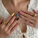 Close-up of hands with colorful nail art and gold rings on a light background