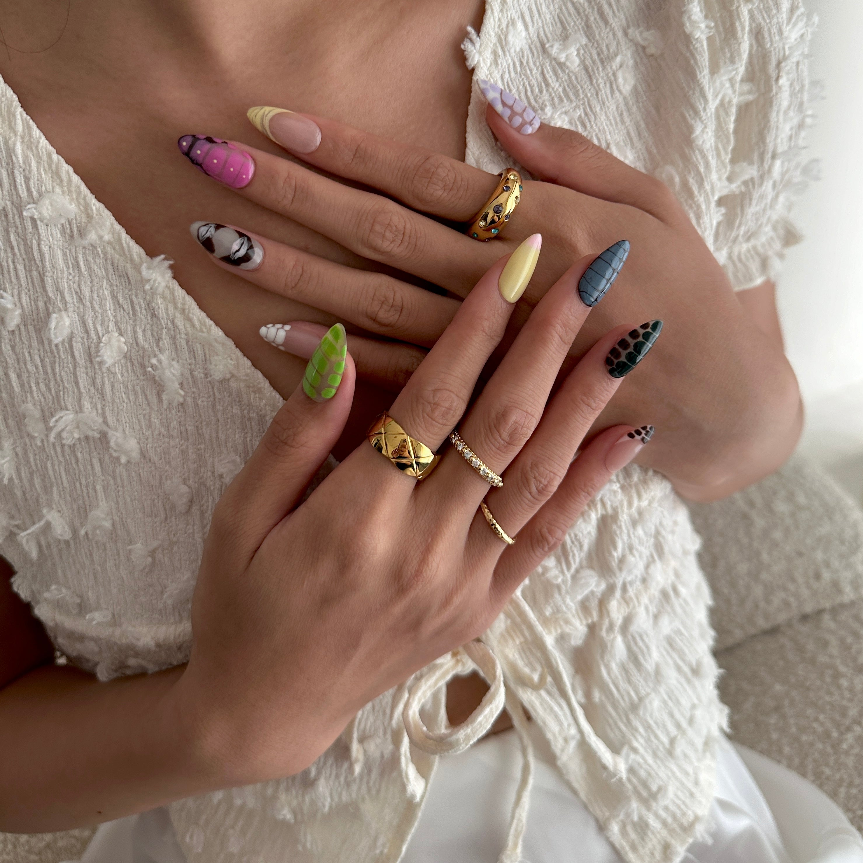 Close-up of a hand with colorful nail polish and multiple rings, wearing a white lace top.