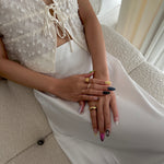 Person wearing a white outfit with lace details and multiple rings on a neutral background