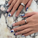 Close-up of hands with blue and white floral nail designs on a marble surface