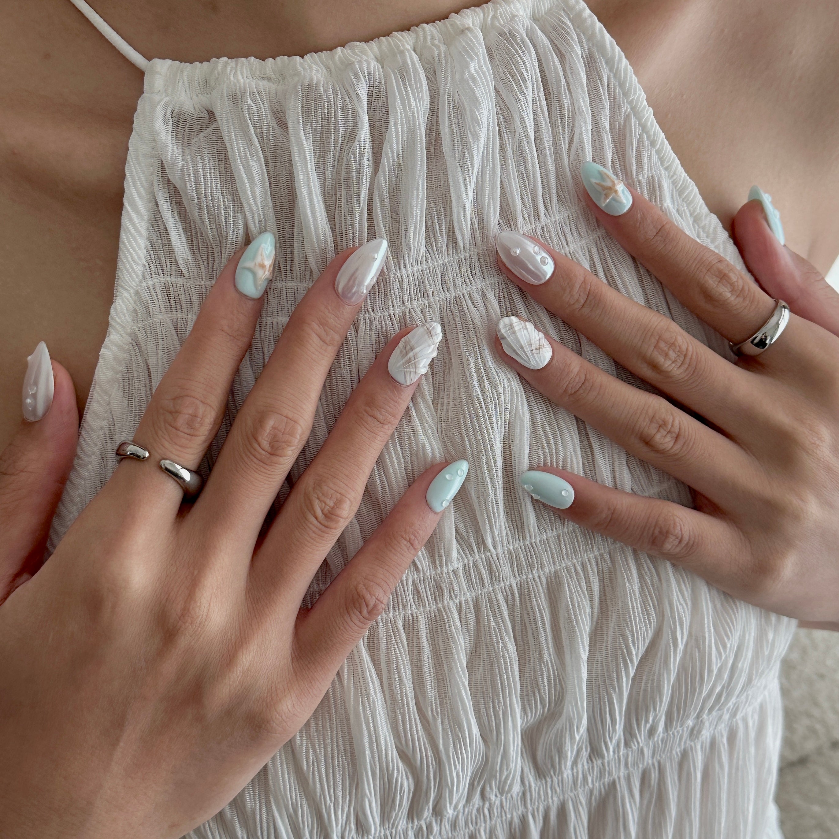 Close-up of hands with light nail polish and rings on a textured white fabric background