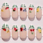 Press on nail art with various designs including strawberries, ladybugs, and flowers on a white background.