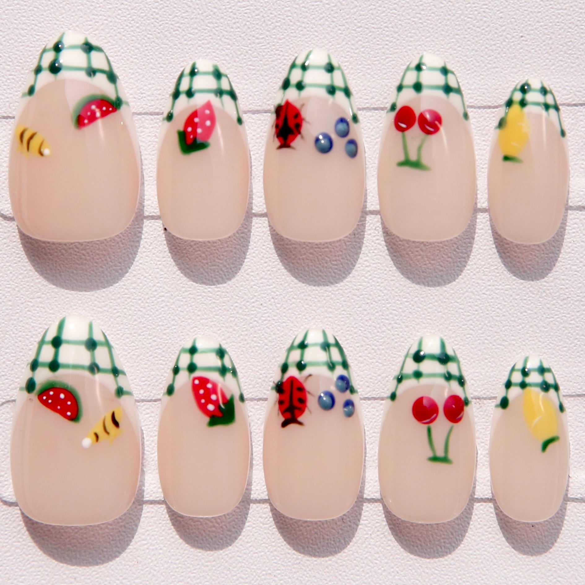 Press on nail art with various designs including strawberries, ladybugs, and flowers on a white background.