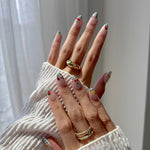 Close-up of hands with press on nails and rings against a neutral background