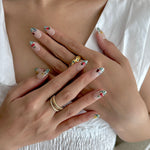 Close-up of hands with decorative nail art and gold rings on a white background